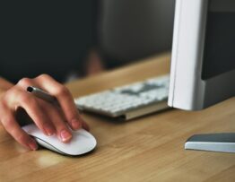 Free A hand using a wireless mouse at a modern desk setup with a computer and keyboard. Stock Photo