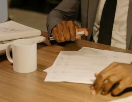 Free Close-up of a businessman holding and reviewing documents on a wooden desk. Stock Photo